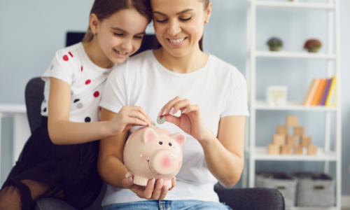mother helping daughter put coins in piggy bank