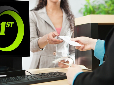 A person standing behind a desk and handing a document to another person