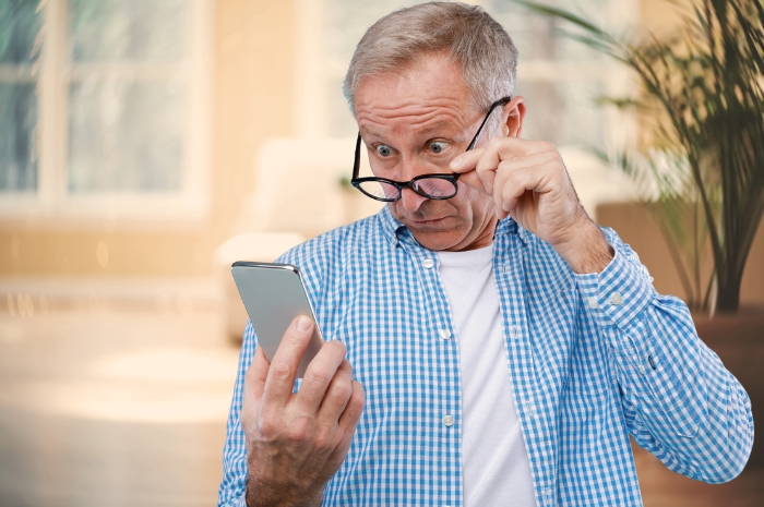 a middle-aged man adjusts his glasses while looking at his phone in surprise