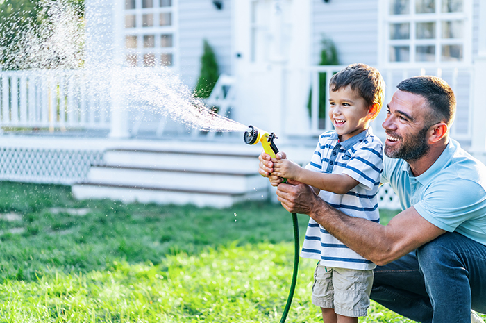 father helping young son water the grass in backyard of their home