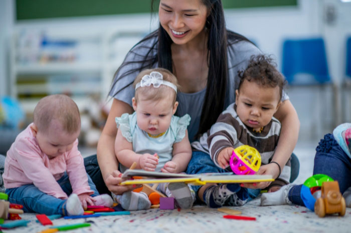 daycare teacher playing on the floor with three small children