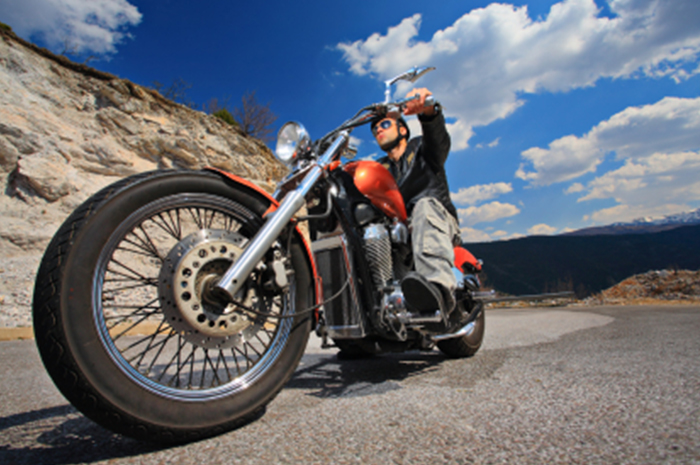 motorcycle and rider on a highway with blue sky and bluffs in background