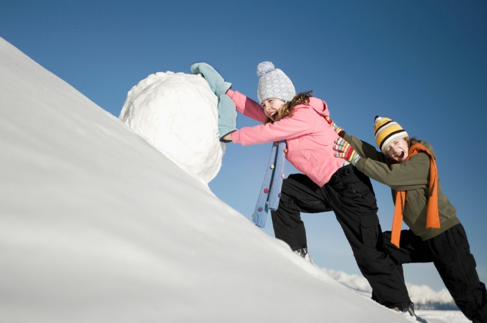 two children pushing a huge snowball up steep hill